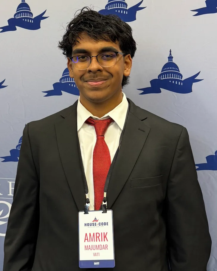 Me in a suit wearing my House of Code badge, in front of a backdrop printed with the U.S. Capitol